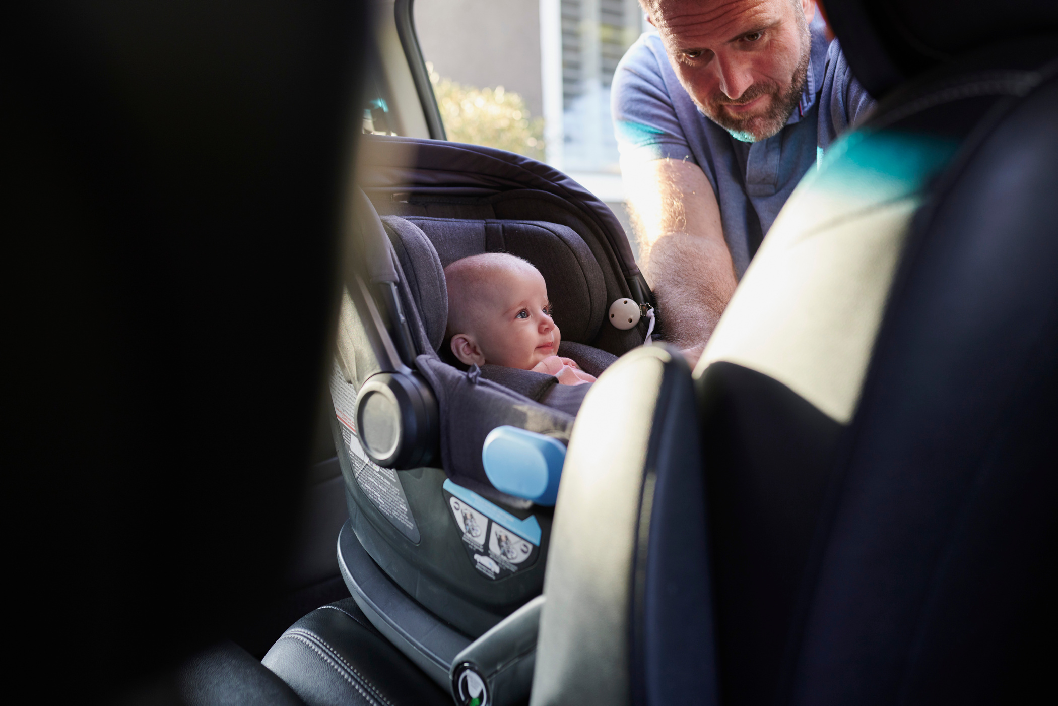 Father fastening baby girl into car safety seat